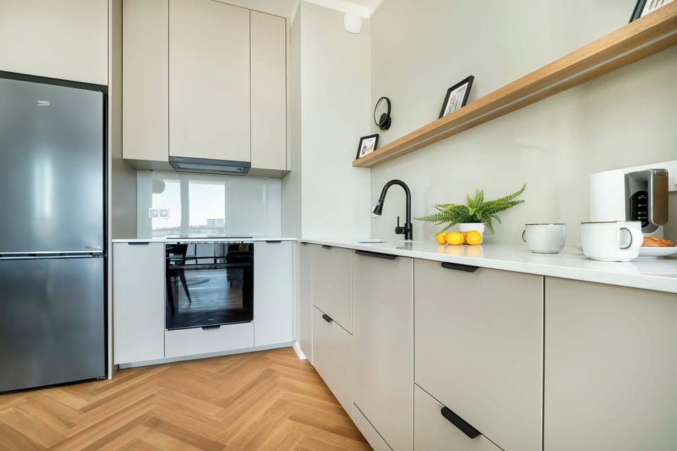 White and functional kitchenette with an oven, a kettle, a fridge, and a dishwasher.