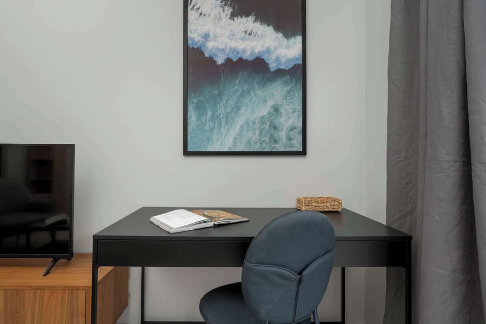 A media unit with a mounted TV, contemporary artwork above, and a workspace with a desk and chair in the corner.

