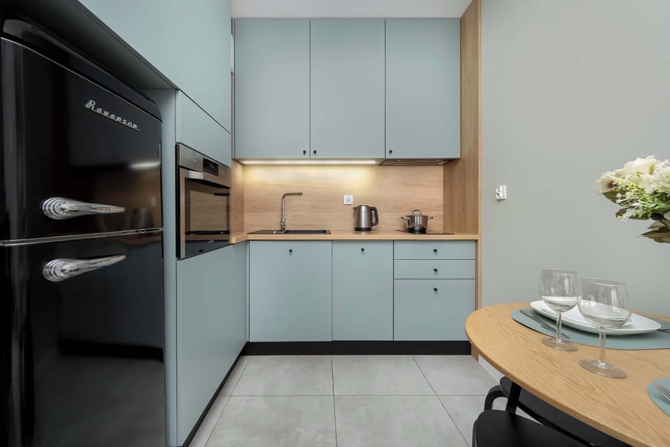 A sleek kitchenette with matte blue cabinets, wooden accents, and essential appliances for everyday cooking.