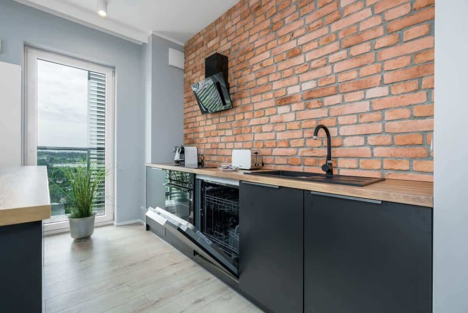 A modern kitchen featuring a brick accent wall, black cabinets, and a sleek induction cooktop with appliances neatly arranged.