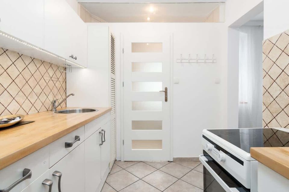 A hallway leading to the kitchen, featuring white cabinetry, modern lighting, and wooden countertops.

