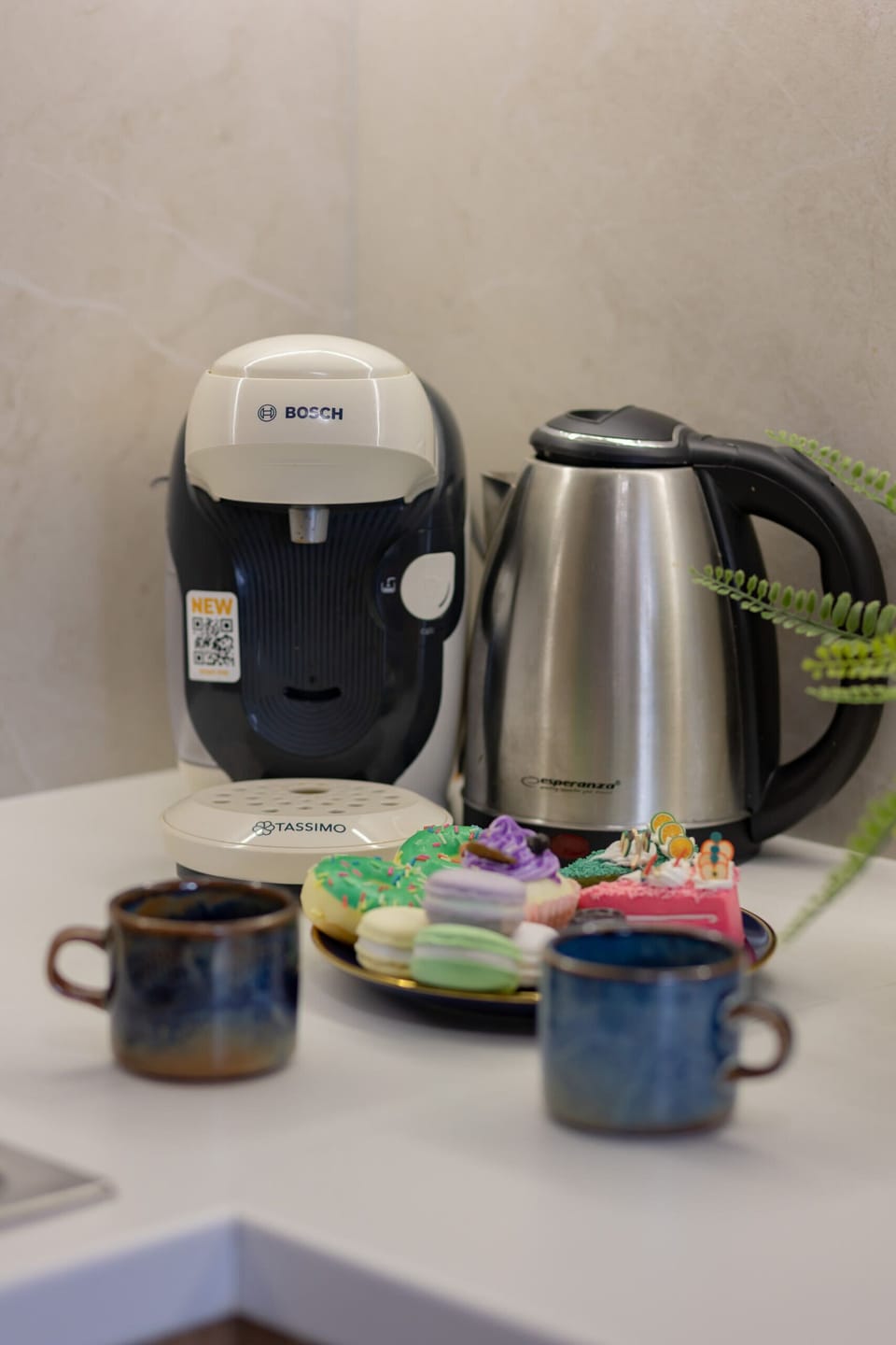 A tea and coffee setup on a white counter, including a kettle and cups. A stylish tray organizes the items neatly.