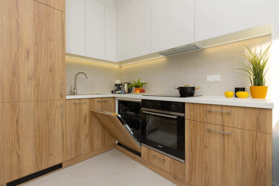 A kitchen corner with wooden cabinets and a black countertop, equipped with a modern stove and a small potted plant. The lighting is bright and even.