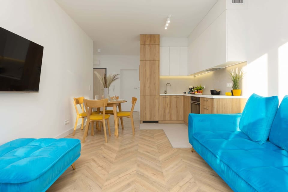 A kitchen and living space featuring modern furniture, including a blue sofa and a wooden dining table. The layout is open and inviting.