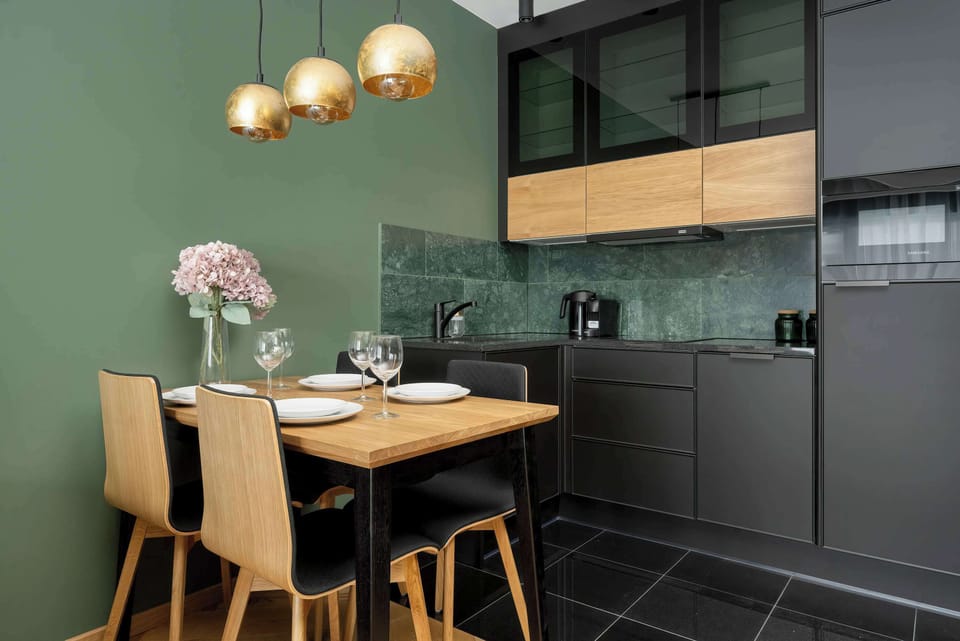 A functional kitchen with black and wood cabinetry, a countertop, and built-in appliances. The design is sleek and modern, blending seamlessly with the dining space.