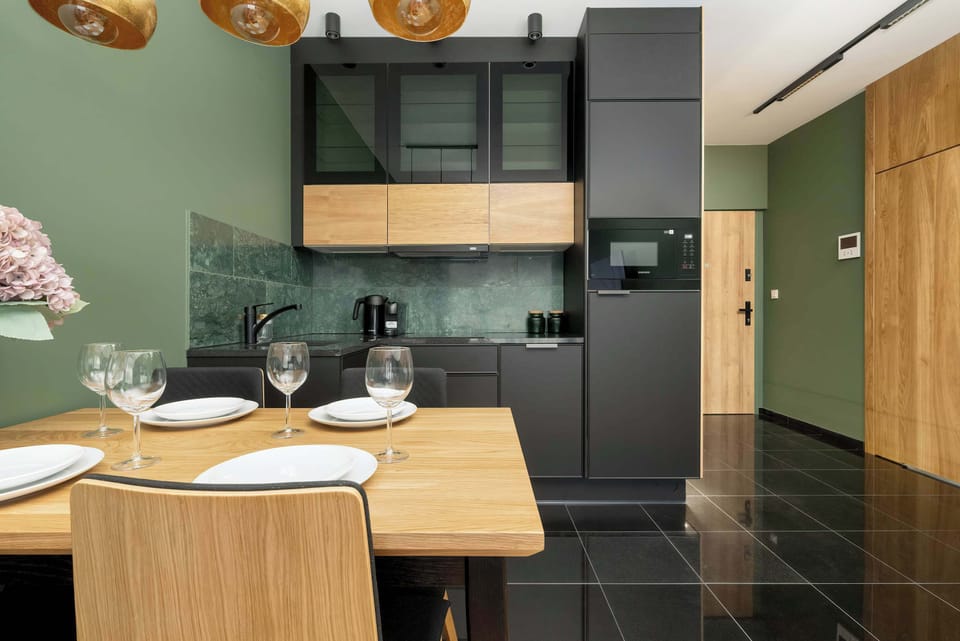 Another view of the kitchen, focusing on the combination of green walls, black cabinetry, and gold lighting fixtures. The table is set for dining, adding a welcoming touch.