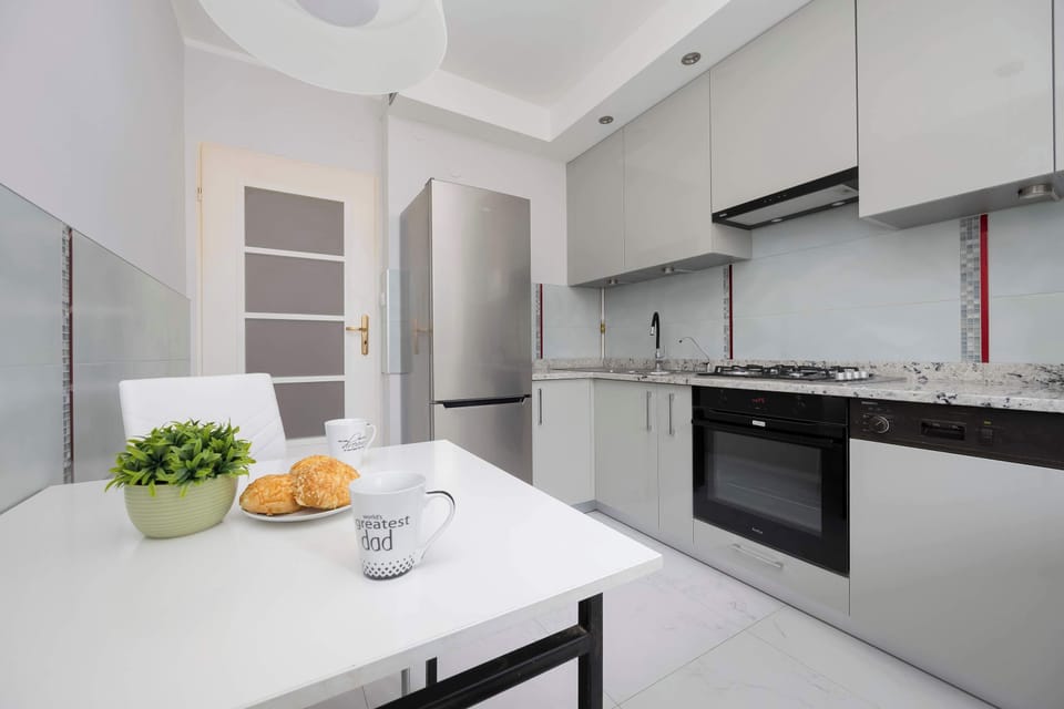 A sleek, modern kitchen with white cabinets, a marble countertop, and built-in appliances.