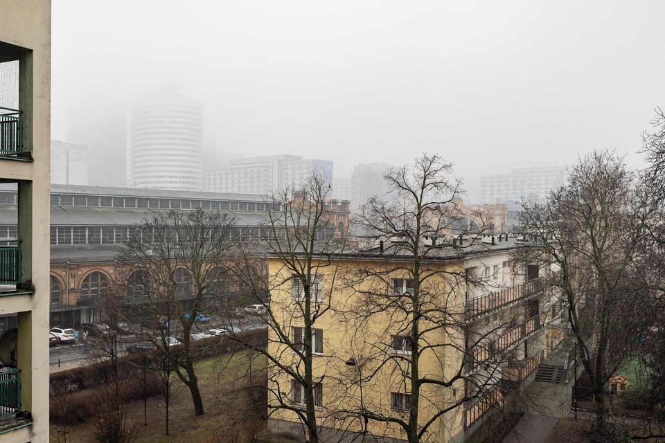 A foggy view from the window showing bare trees and urban surroundings.