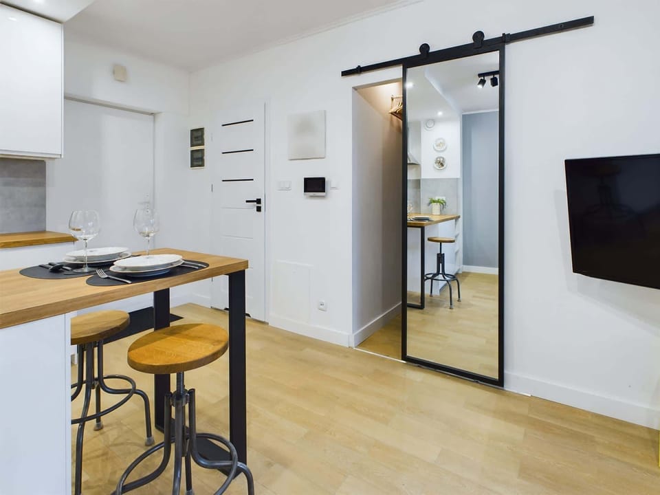 The bright, airy space of the flat. In the photo you can see the two bar chairs by the wooden countertop and the door leading to the dressing room. To the left, a large television hangs on the wall.