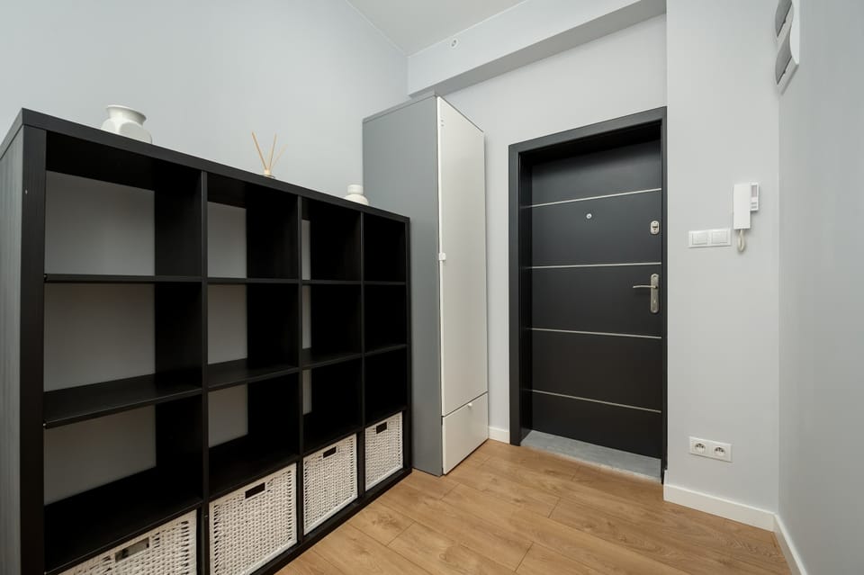 A hallway view with open black shelving units and a door leading into the apartment.