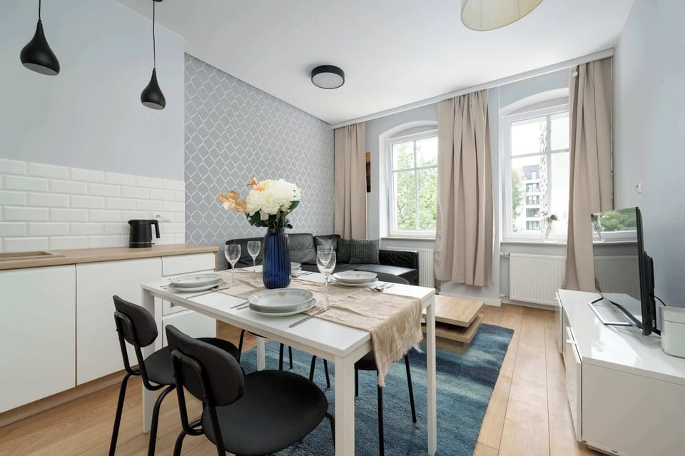 A modern dining space with a table set for four, adjacent to a white kitchenette with upper and lower cabinets.