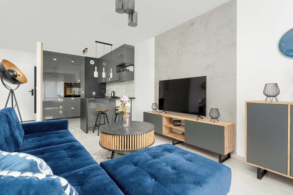 Living room with a large blue sectional sofa, a wooden coffee table, a flat-screen TV mounted on the wall.