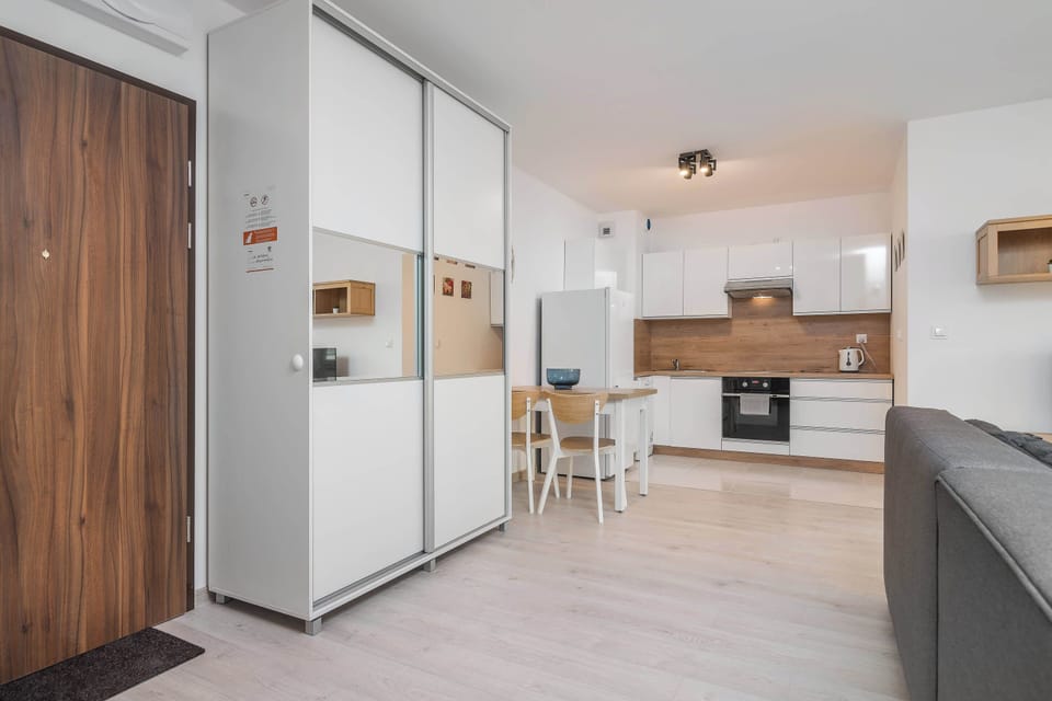 The open-plan kitchen is visible in the background, with white cabinets and a light wood finish, while a large mirrored wardrobe is prominent in the foreground.