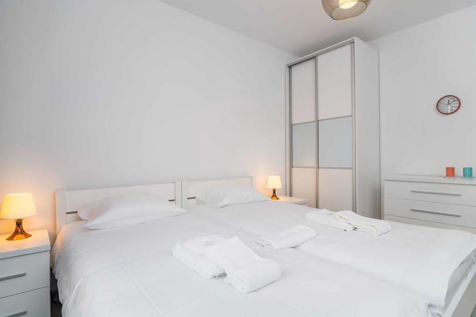 A bright bedroom with a double bed made up with white bedding, nightstands, and a large wardrobe with mirrors.