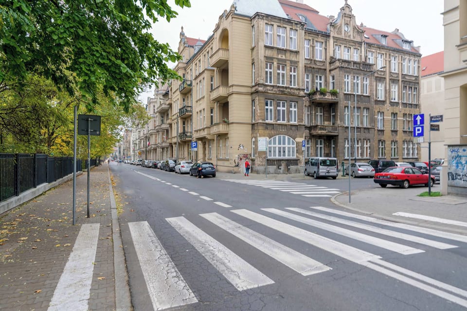 A shot of the surrounding street and buildings with crosswalks and parked cars.