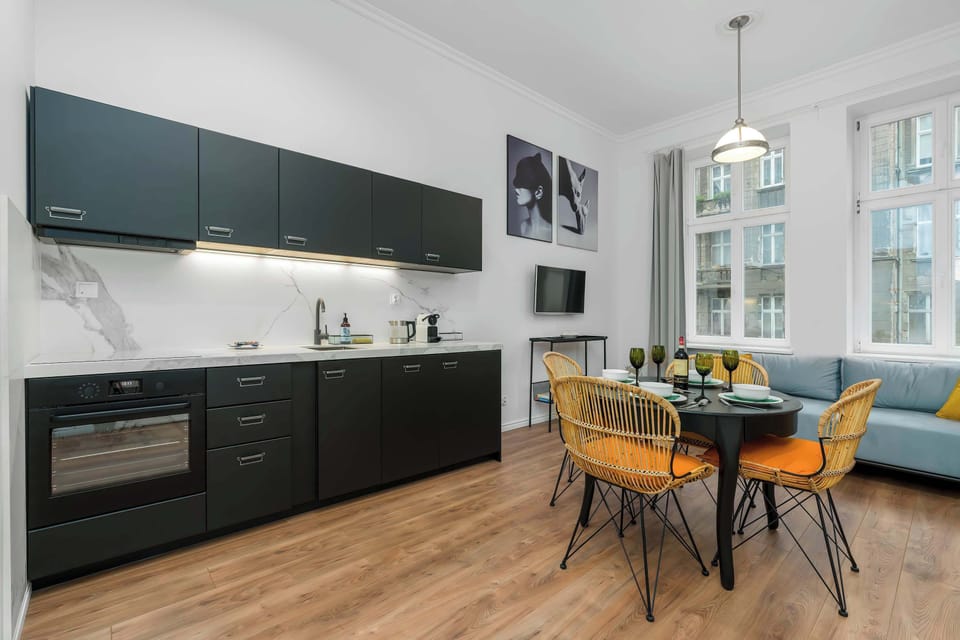 A sleek kitchen with black cabinets, a wooden dining table with yellow chairs, and modern lighting.