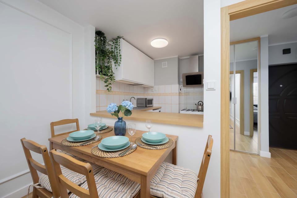 A wooden dining table with four chairs, set with plates and glasses, positioned near the kitchen.