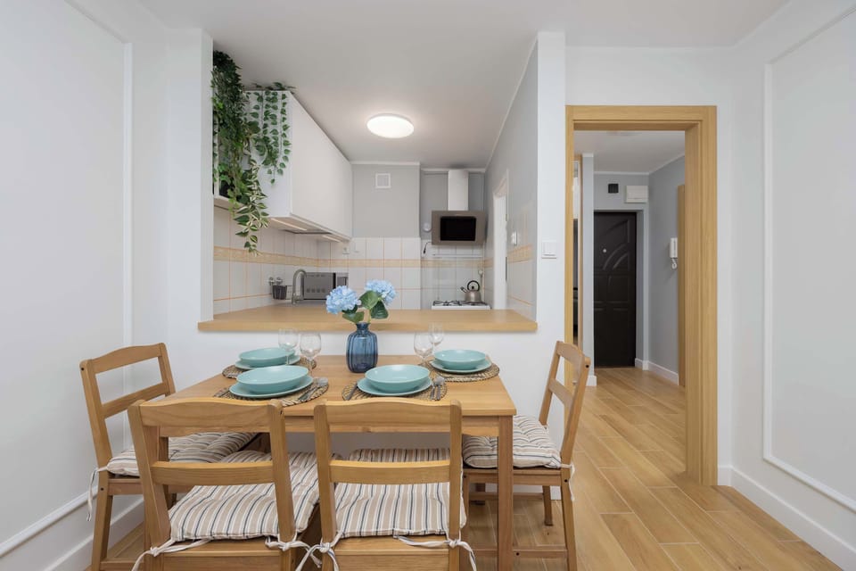A wooden dining table with four chairs, set with plates and glasses, positioned near the kitchen.