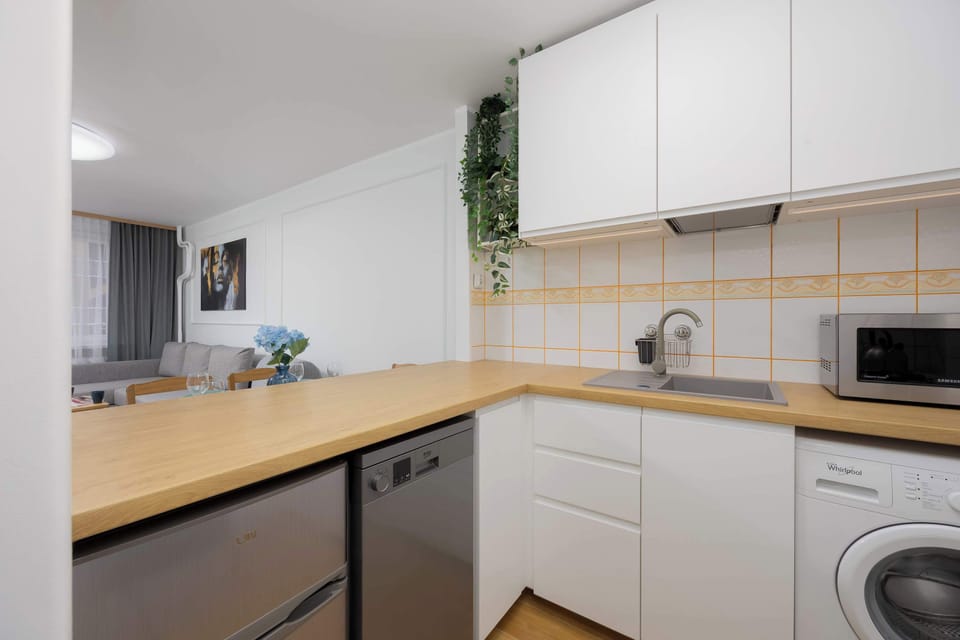 A compact kitchen with white cabinets, wooden countertops, and modern appliances, including a washing machine and a microwave.