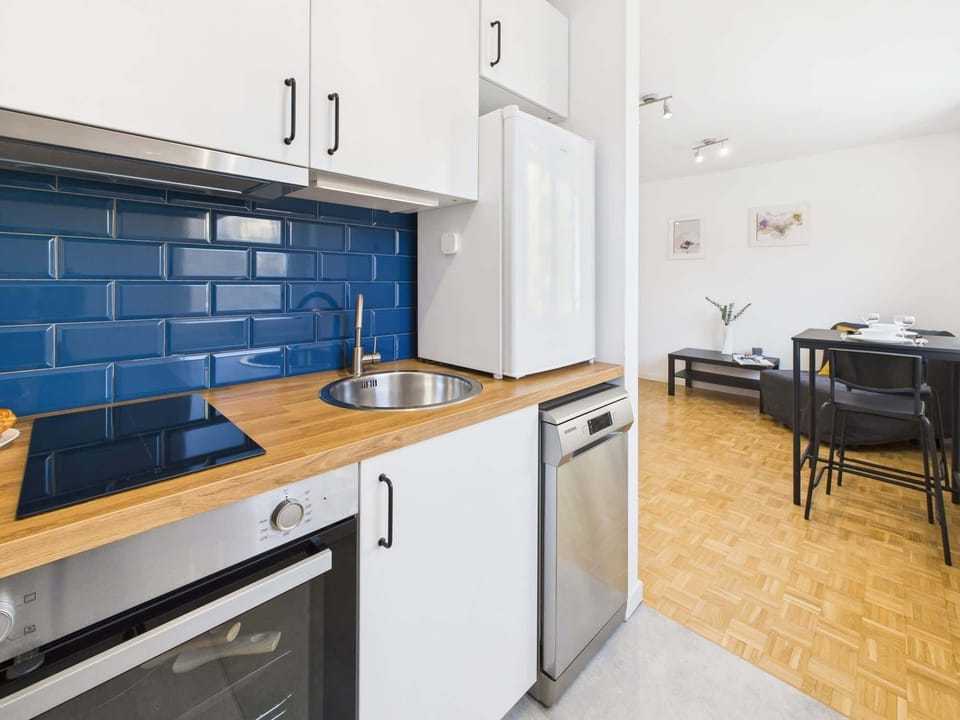 A stylish kitchenette with white cabinets, a wooden countertop, and a beautiful blue tiled backsplash, offering a sleek and functional space.