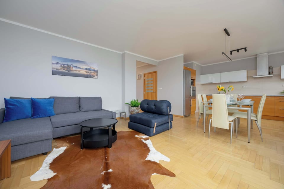 A corner view of the main living space, combining the kitchen, dining, and sitting areas with wooden parquet flooring.