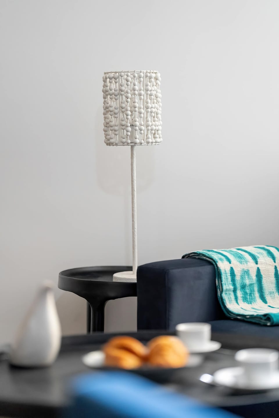 Close-up of a sofa and a black table with a white lamp standing next to it.