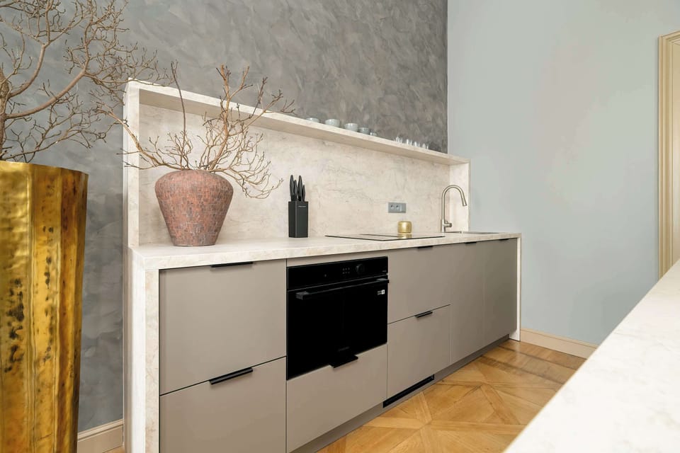 A modern kitchen with a sleek marble countertop, gold accents, and barstools arranged neatly.