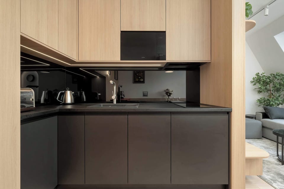 A compact kitchen area featuring matte black and light wood cabinets, with a modern induction cooktop and under-cabinet lighting.