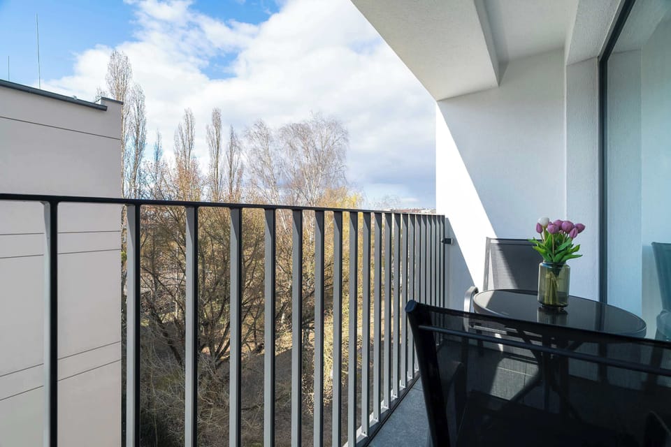 A balcony with a black railing and a small table, offering a pleasant outdoor space with a view of trees.