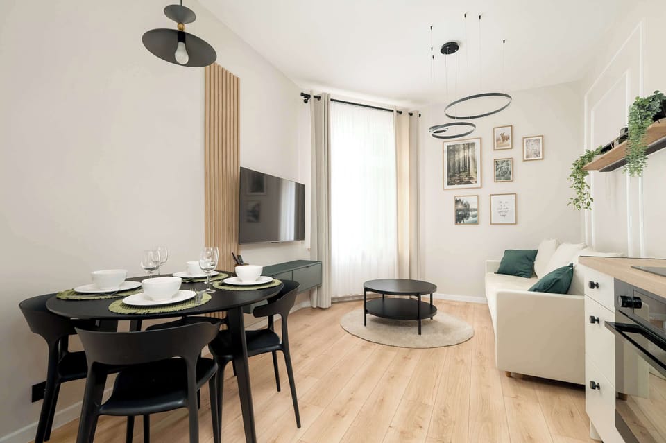 An open-plan living room with a dining table and a comfortable seating area. Light wood flooring and simple decor create a welcoming space.
