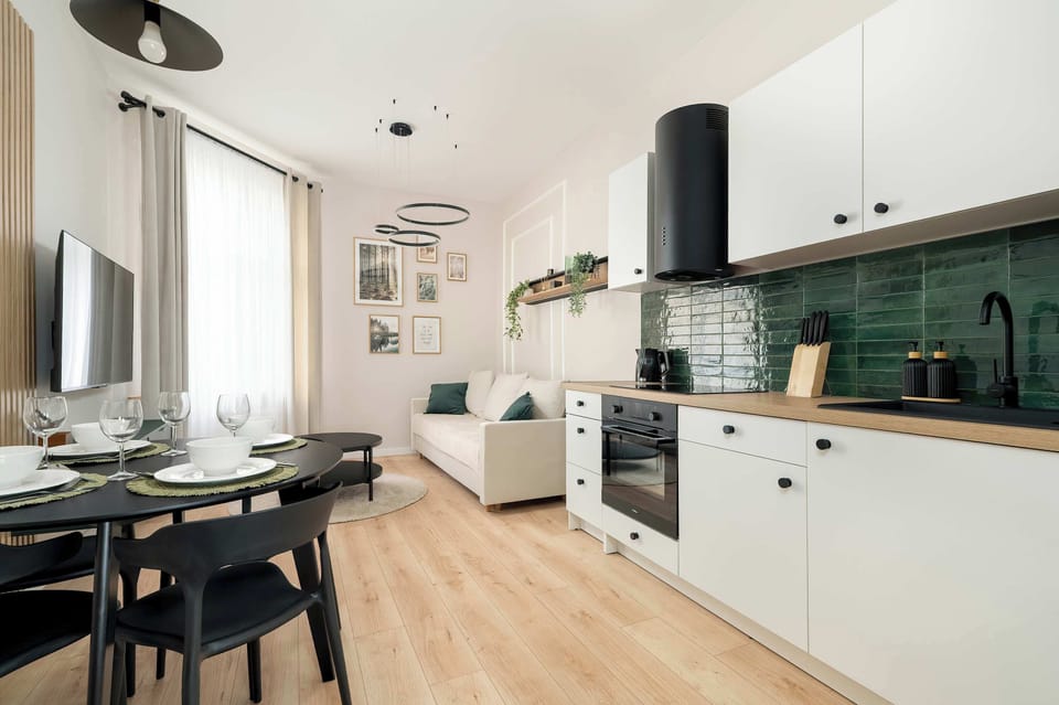 A shared space combining a cozy living room and a well-equipped kitchen. Green tile backsplash and dark cabinetry add a bold touch.