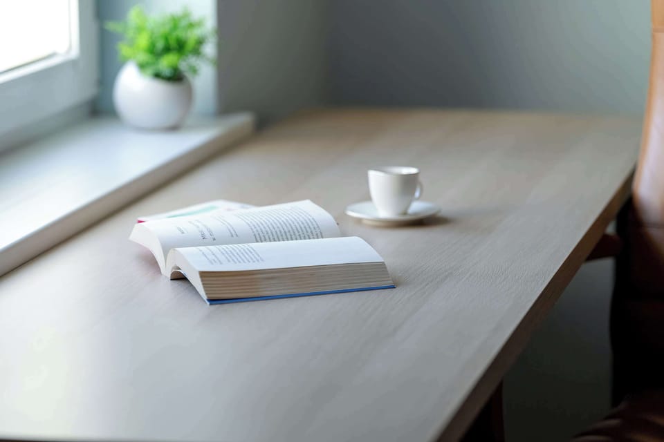 A minimalistic desk setup with a white mug and book, capturing a peaceful, studious atmosphere.