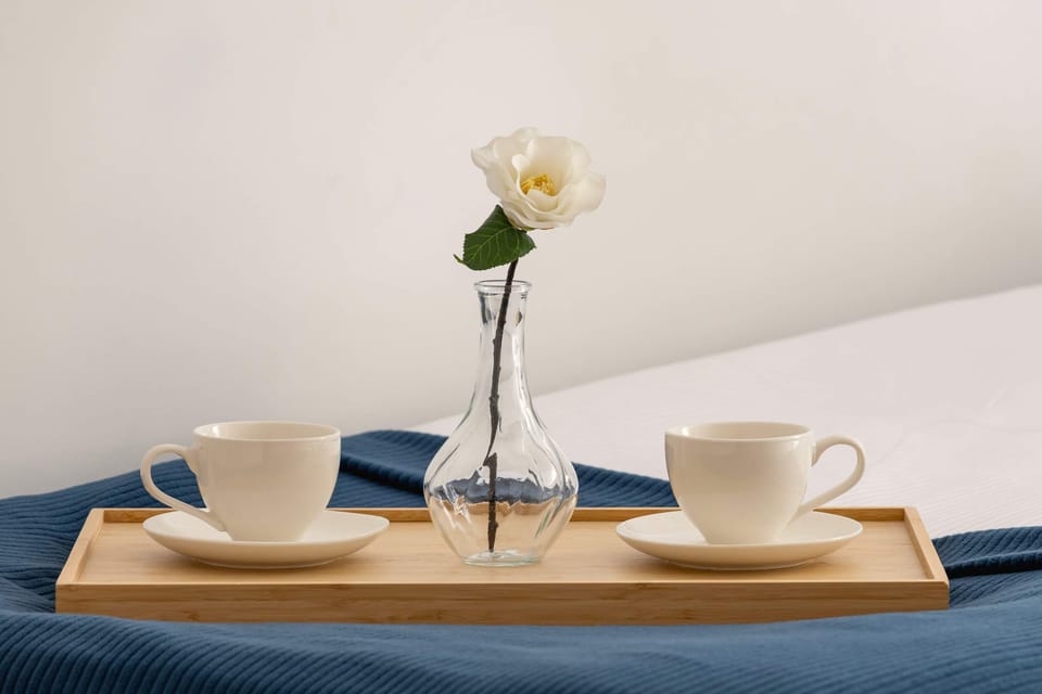 Close-up of a breakfast tray on the bed with two cups and a small flower in a vase, creating a cozy and welcoming atmosphere.