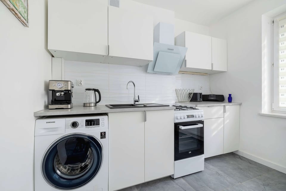 The kitchenette combines functionality with modern style, featuring a washing machine, oven, and ample storage. Bright cabinetry and a minimalist design create a harmonious, practical space.