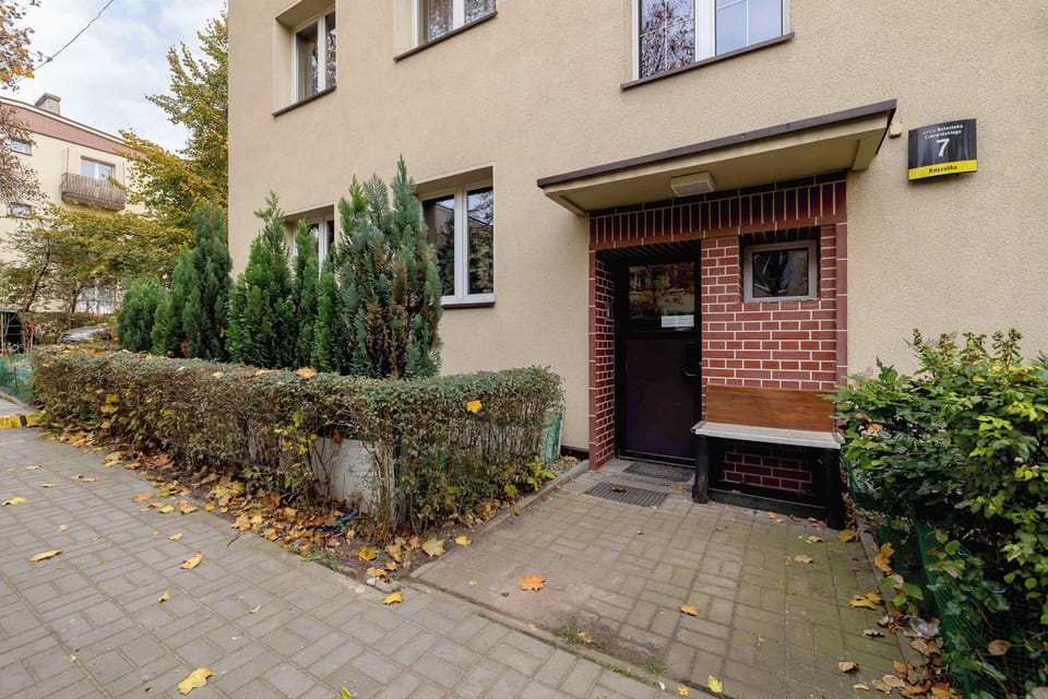 The exterior of the building shows a traditional design with a brick pathway leading to the entrance. The surrounding greenery adds a welcoming touch.