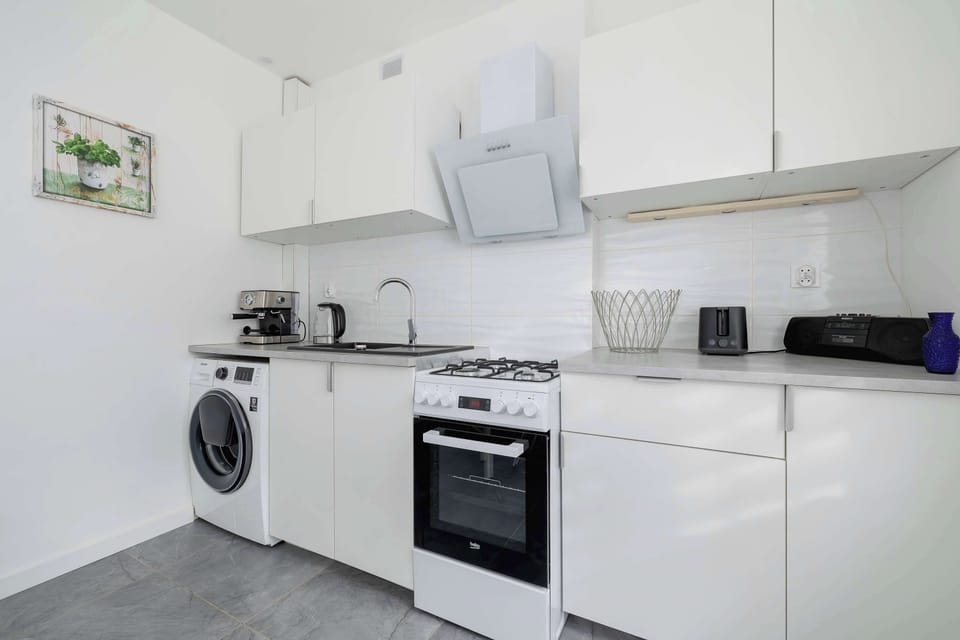 The kitchen area is equipped with a washing machine, an oven, and plenty of countertop space. White cabinets provide a clean and minimalist look.