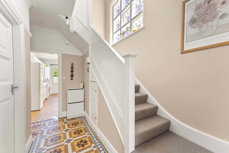 The entrance hall combines traditional patterned floor tiles with a modern neutral palette, leading to a crisp white staircase with integrated storage.
