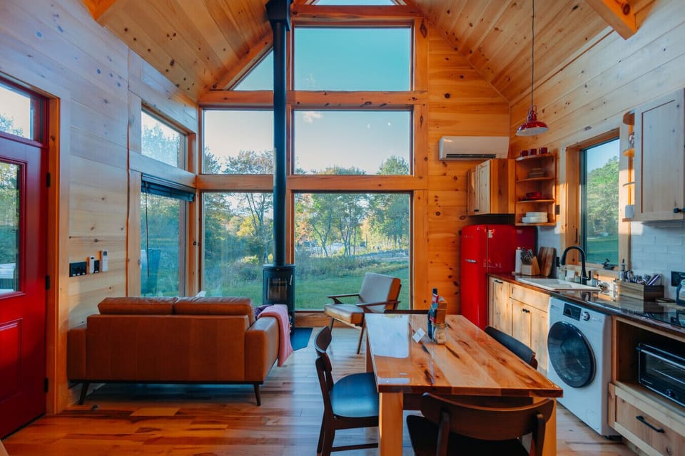 Morning light fills the Cherry Cabin’s living room and kitchen, with views of the trees and river beyond.