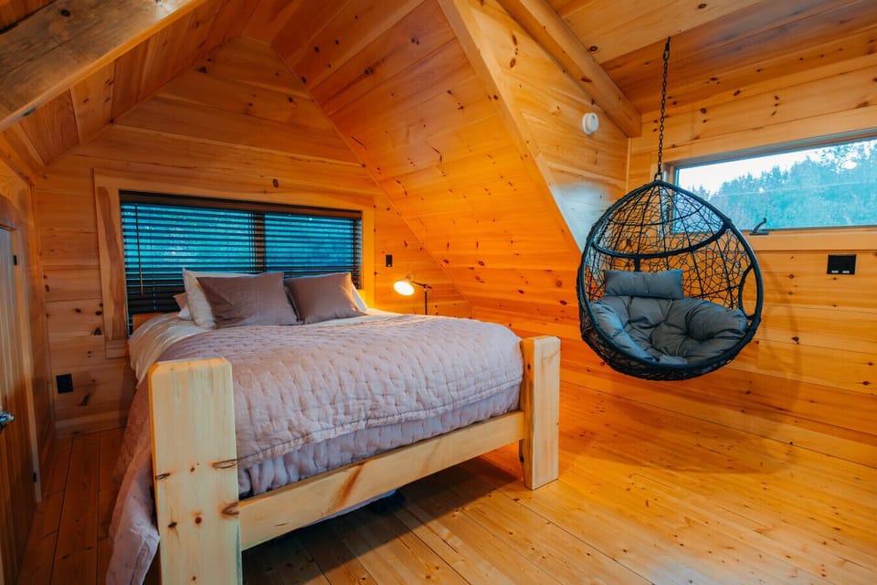 Queen bed and hanging chair in the Cherry Cabin loft, surrounded by warm pine walls and soft evening light.