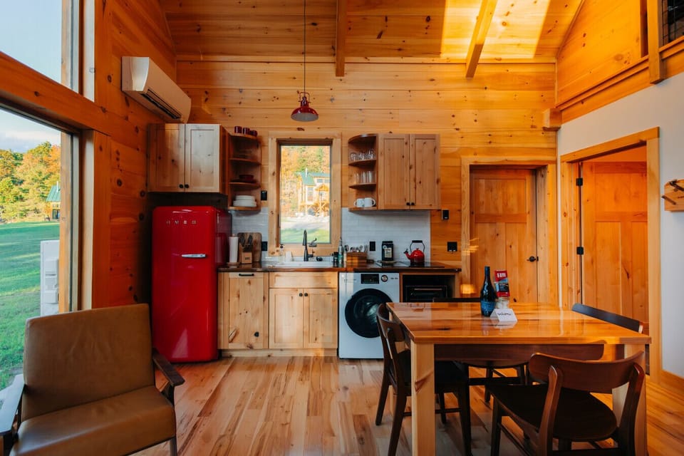 Kitchen and dining area of the Cherry Cabin, featuring natural pine, red accents, and morning light through the window.