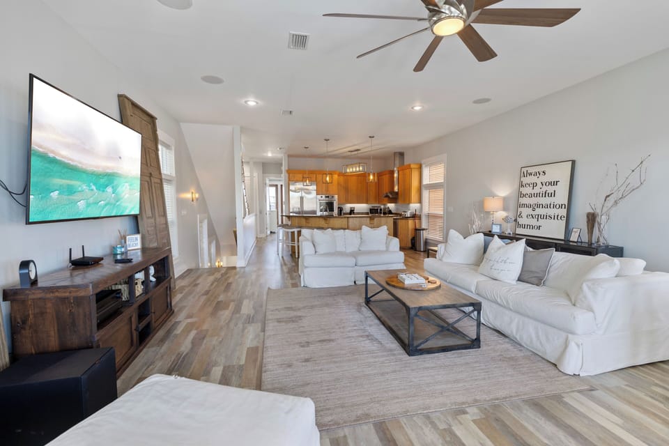 Relax in your spacious living room where modern comfort meets coastal charm, complete with plush seating and ocean views on TV.