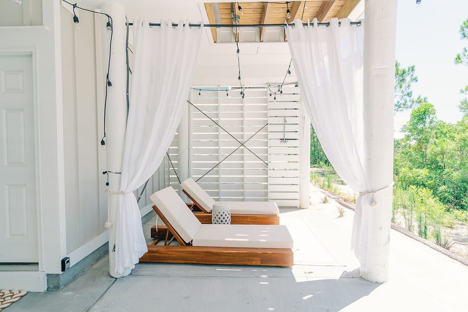 cushioned lounge chairs framed by airy white curtains and soft string lights create a serene outdoor oasis perfect for soaking up the sun or unwinding with a good book.