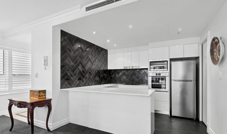 A sleek kitchen featuring white cabinetry and a dark, patterned backsplash.