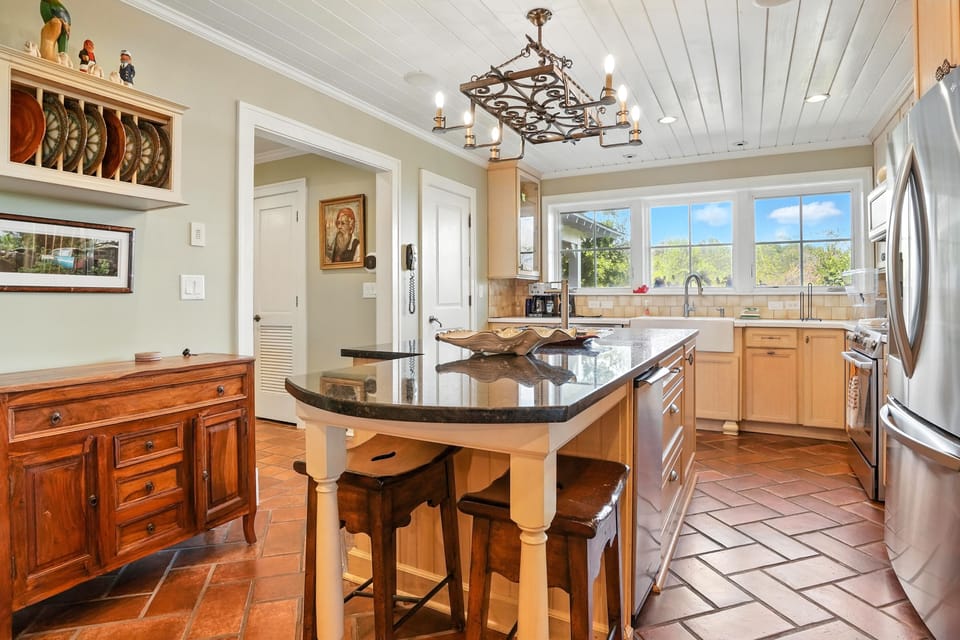 Left Wing Kitchen • Island Seating + Picture Window - This additional angle of the downstairs kitchen in the left wing highlights the curved island with bar seating, full-size stainless appliances, and marsh-facing picture window for natural light.