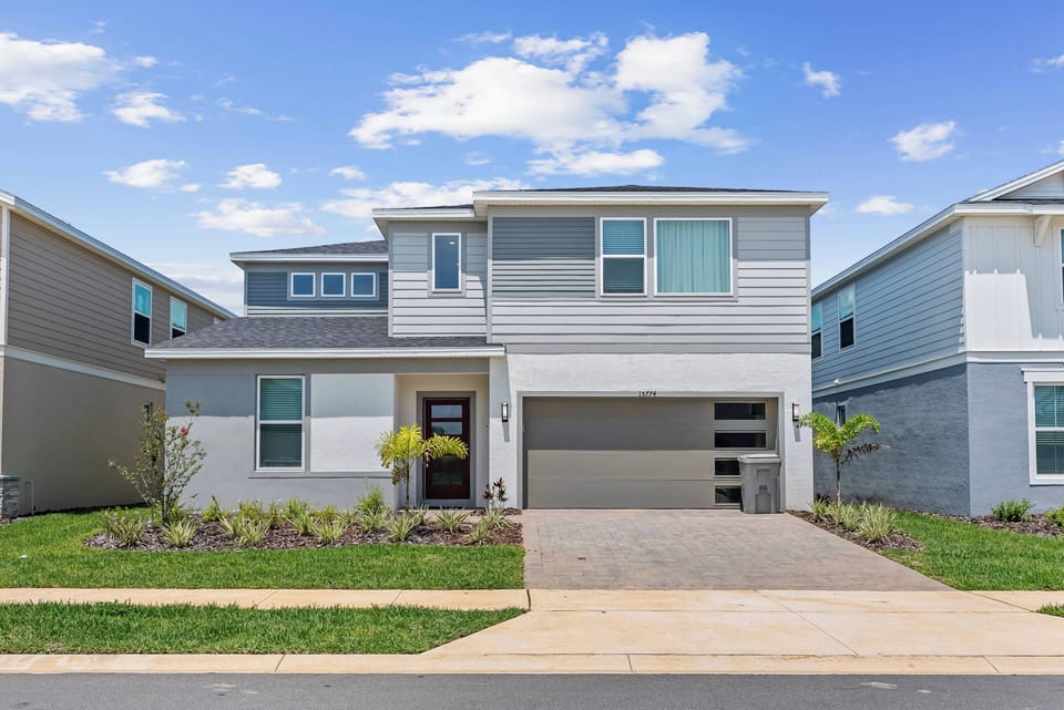 Welcome to this beautifully designed home with modern gray siding and large windows that fill the space with natural light. The manicured front yard, surrounded by lush greenery, creates a warm and inviting atmosphere for your.