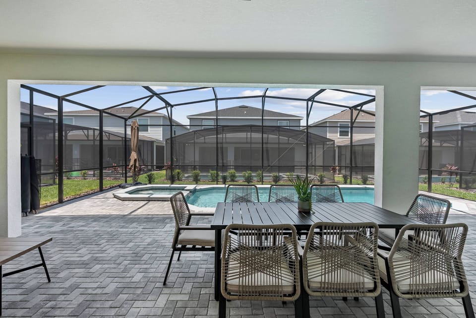 Enjoy outdoor dining on our screened-in patio, featuring a stylish table by the sparkling pool. The sleek pavers and lush greenery create a refreshing atmosphere, ideal for relaxation and memorable meals.