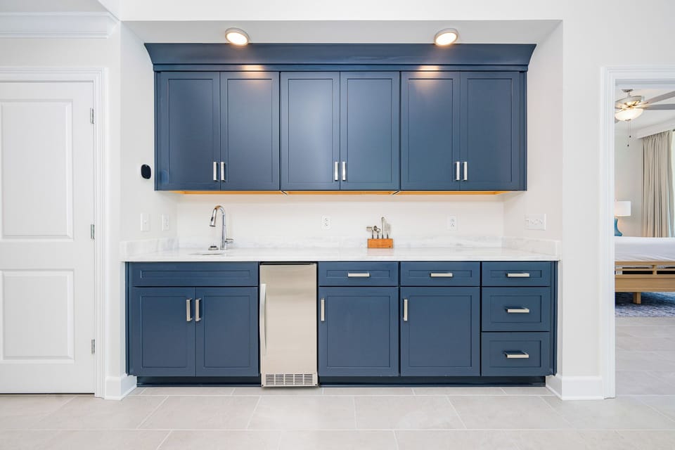 Prepare drinks at this elegant wet bar featuring deep blue cabinetry and a sleek countertop