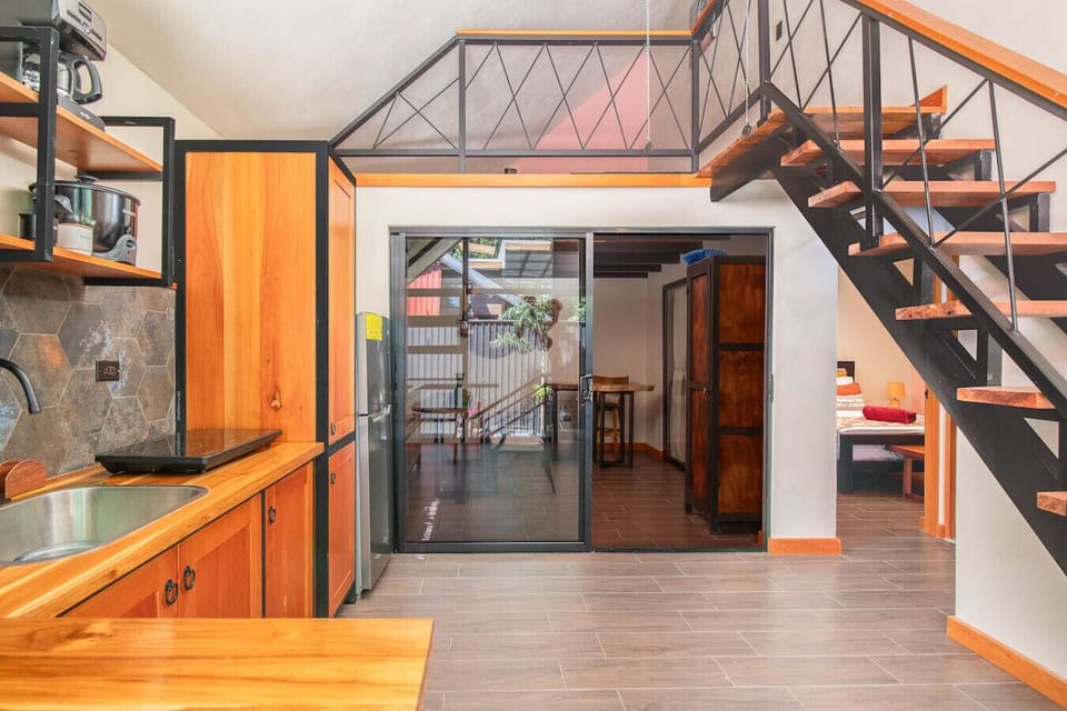 Open-concept living area with kitchen, staircase to mezzanine, and access to outdoor terrace, Aloki Kiré 2, Playa Chiquita, Costa Rica.