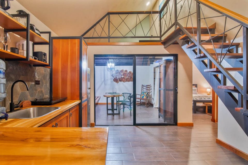 Open-plan kitchen with wooden finishes, mezzanine access, and a view toward the bedroom and terrace area, Aloki Kalok 3 in Playa Chiquita