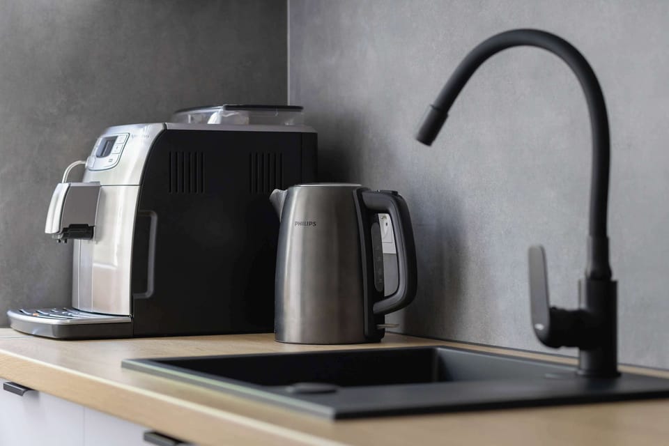 A close-up of a black kitchen faucet and countertop appliances including a coffee machine and electric kettle.